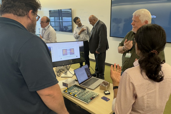 People in a conference room standing around computer hardware and talking.