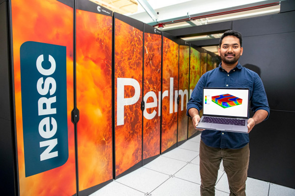 Prabhat Kumar holding a laptop, standing in front of NERSC's Perlmutter supercomputer.