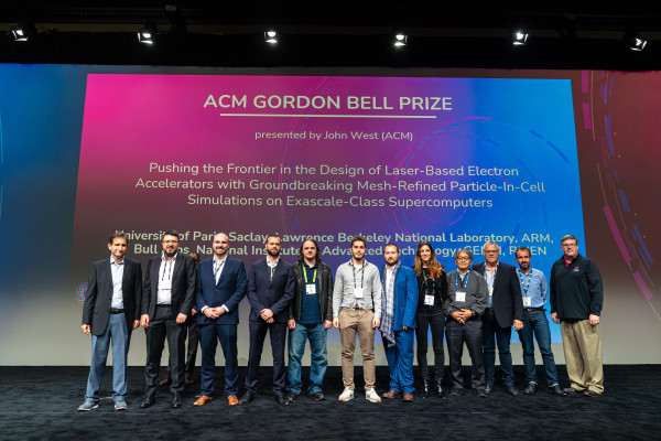 12 people standing on a stage in front of a screen with an image honoring the 2022 winners of the ACM Gordon Bell Prize.